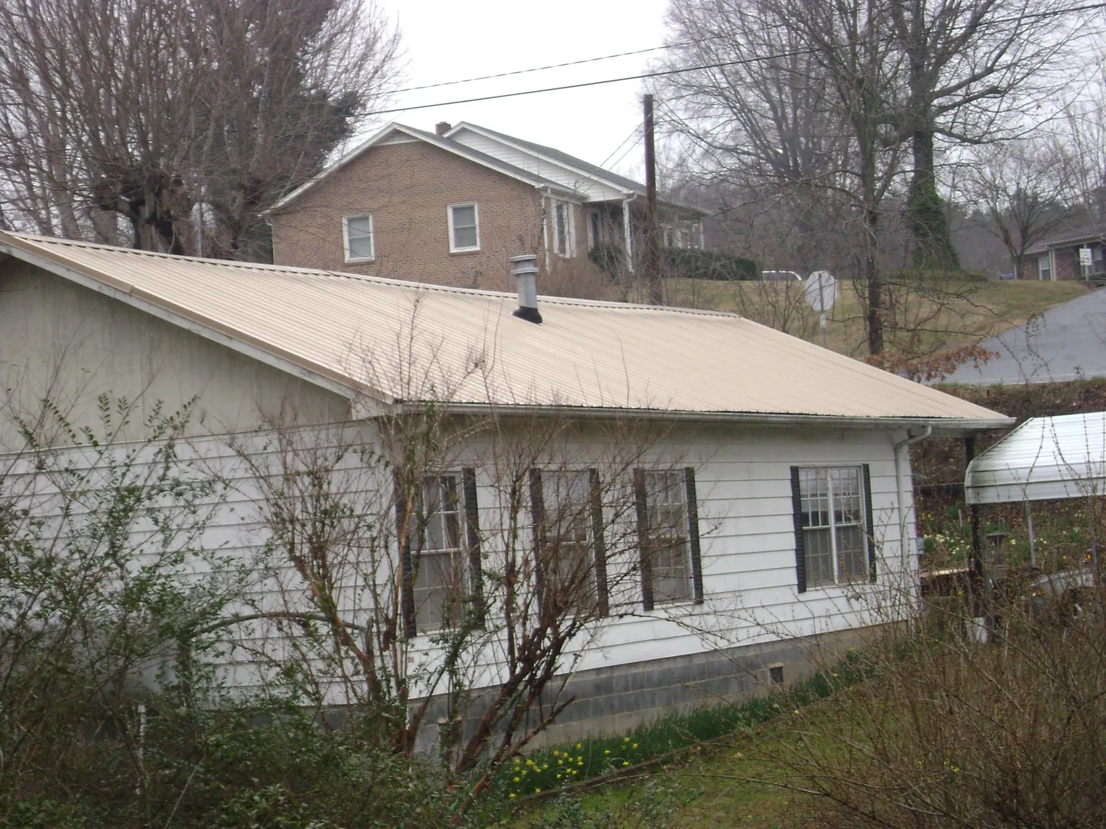 Tan metal roof on a white sided house set into a hillside — Commercial Roofing by Roofing Brothers in Willard